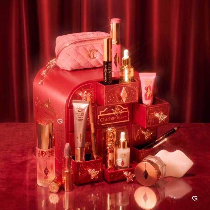 Charlotte Tilbury Advent Calendar 2026 with open jewel-handled drawers, the Pillow Talk charm bag and beauty products on a red backdrop