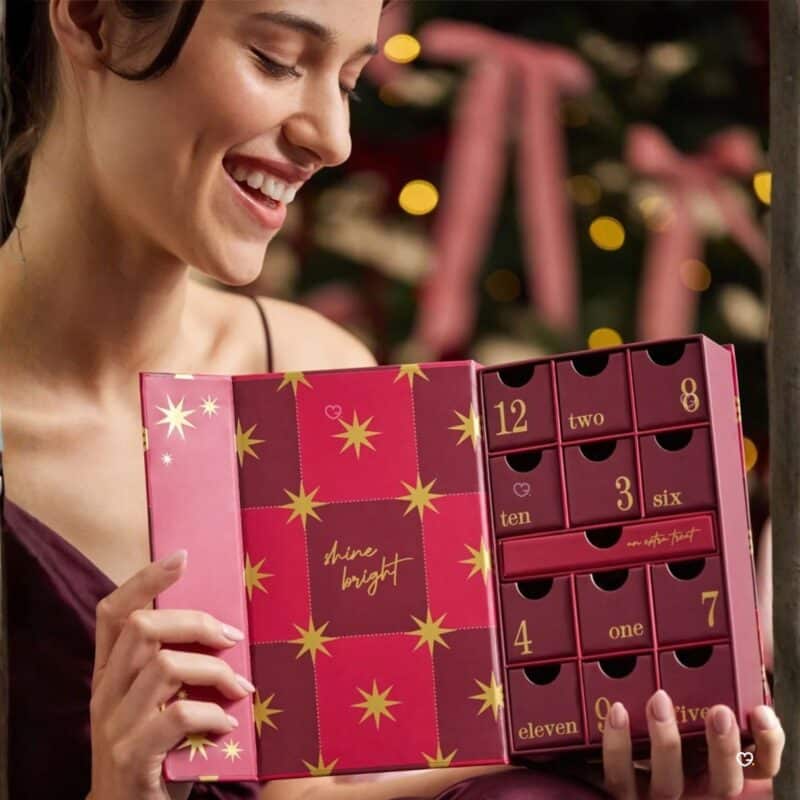 Woman holding the Estella Bartlett gold advent calendar by a Christmas tree