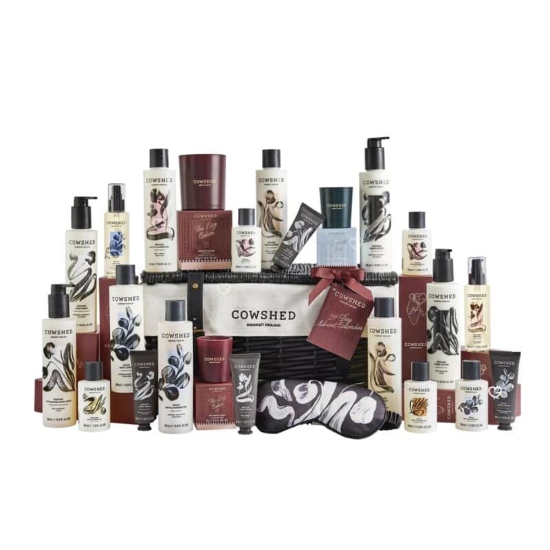 Full lineup of all 24 Cowshed Advent Calendar 2026 products around the wicker hamper on white