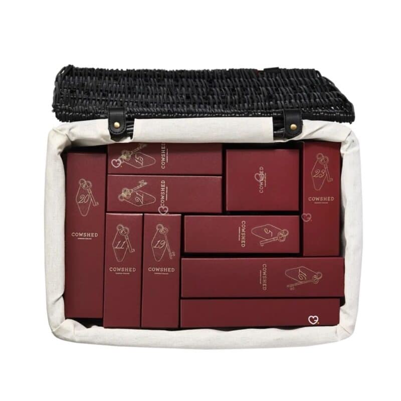 Top-down view of the Cowshed 2026 wicker hamper filled with numbered burgundy gift boxes