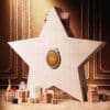 Dior Advent Calendar 2026, closed white star-shaped box with the Dior medallion, on a gold festive backdrop with beauty products
