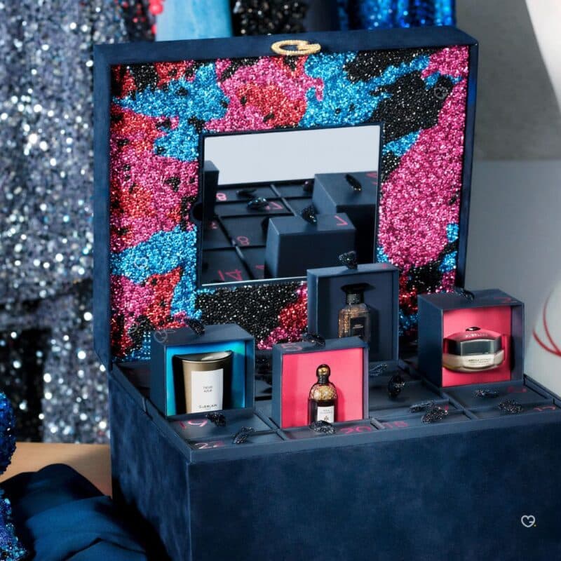 Close-up of the Guerlain Advent Calendar 2026 open, with a Guerlain candle, a Shalimar miniature and an Abeille Royale cream on display